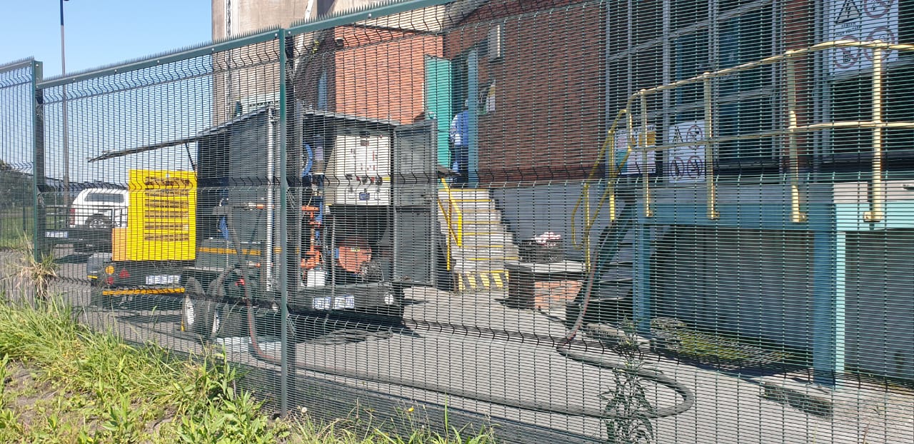 Trailer-mounted generator standing behind a security fence at an industrial site